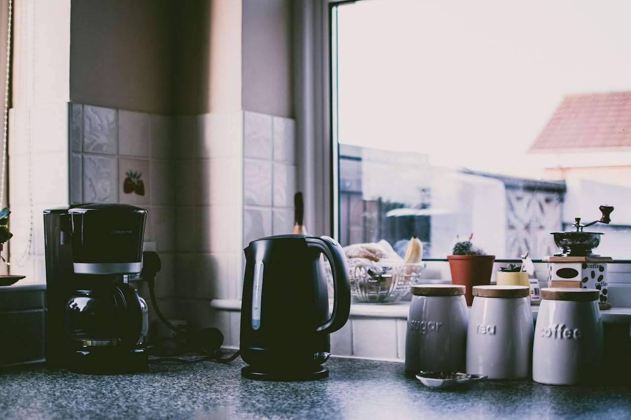 portfolio-04 Cozy kitchen scene with coffee maker, kettle, and jars on a sunny counter.